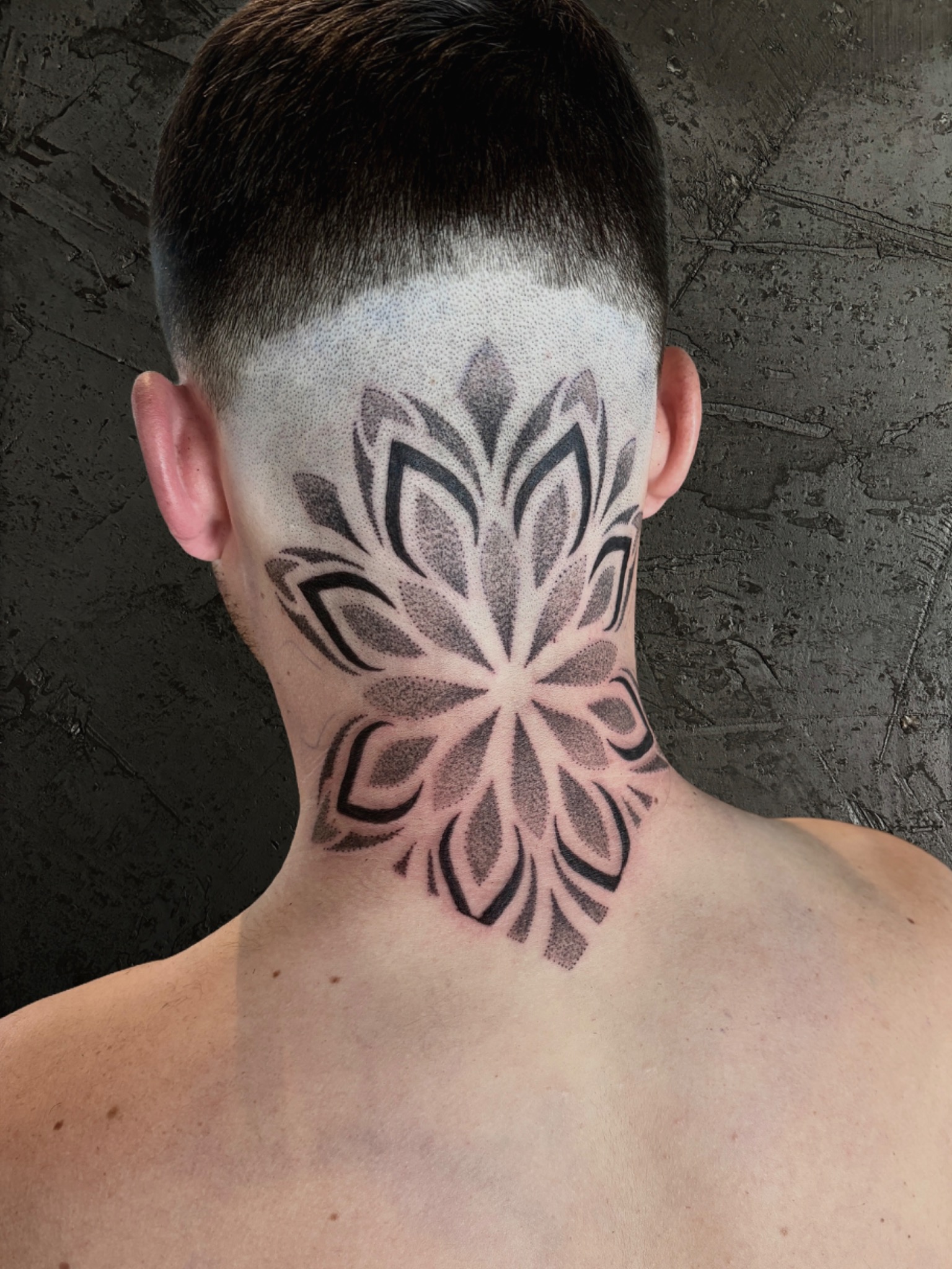 Mandala-Tattoo am Hinterkopf und Nacken mit feinen Punkt-Schattierungen und schwarzen geometrischen Flächen
